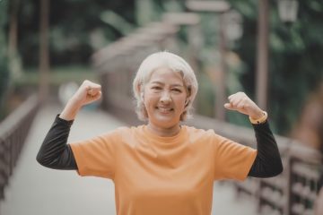 longevity - senior woman flexing muscles outdoors