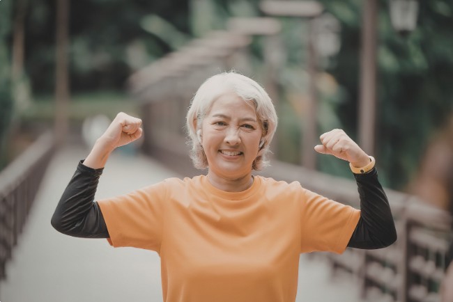 longevity - senior woman flexing muscles outdoors